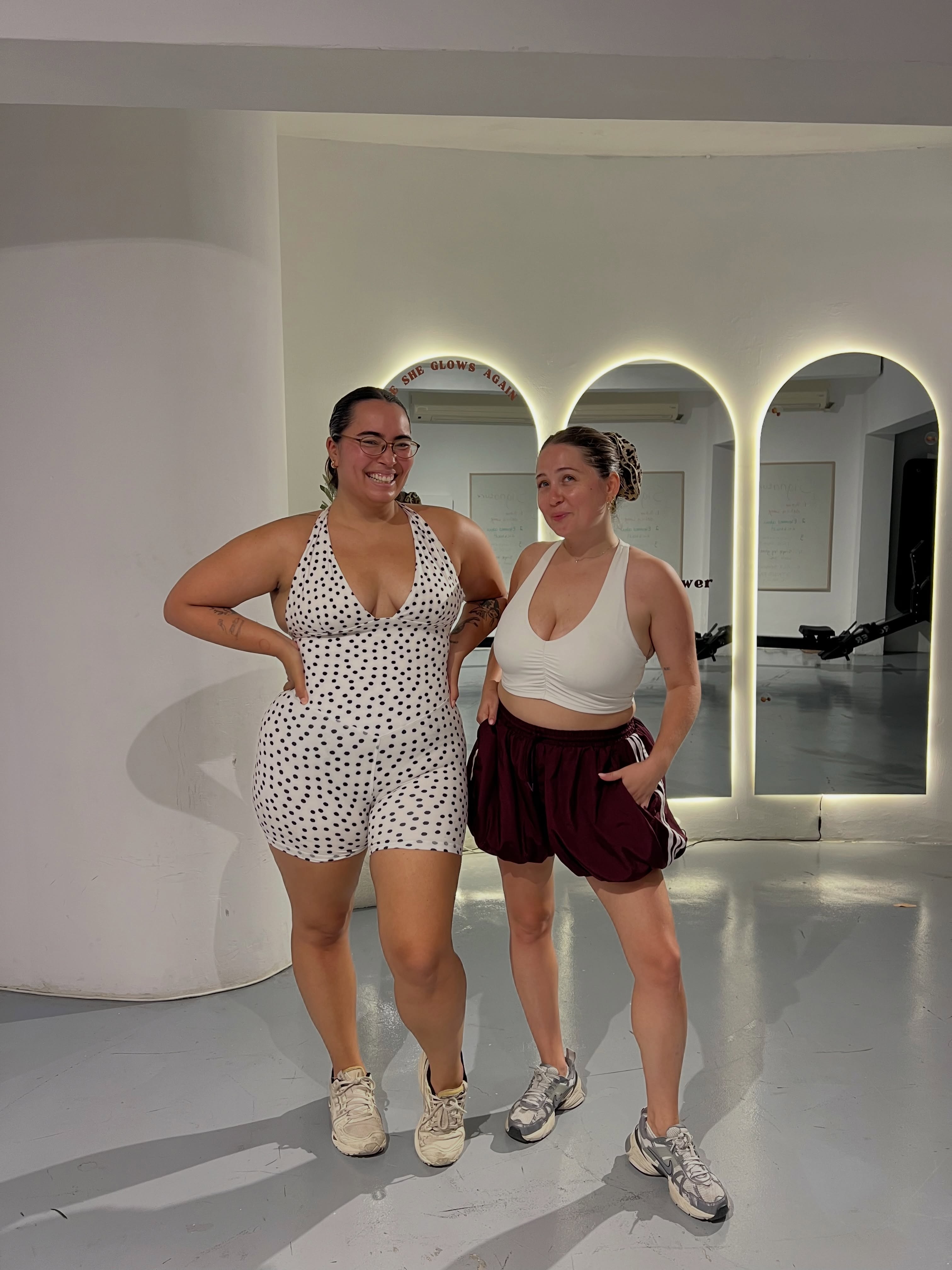 Two women posing in workout attire in front of studio arches